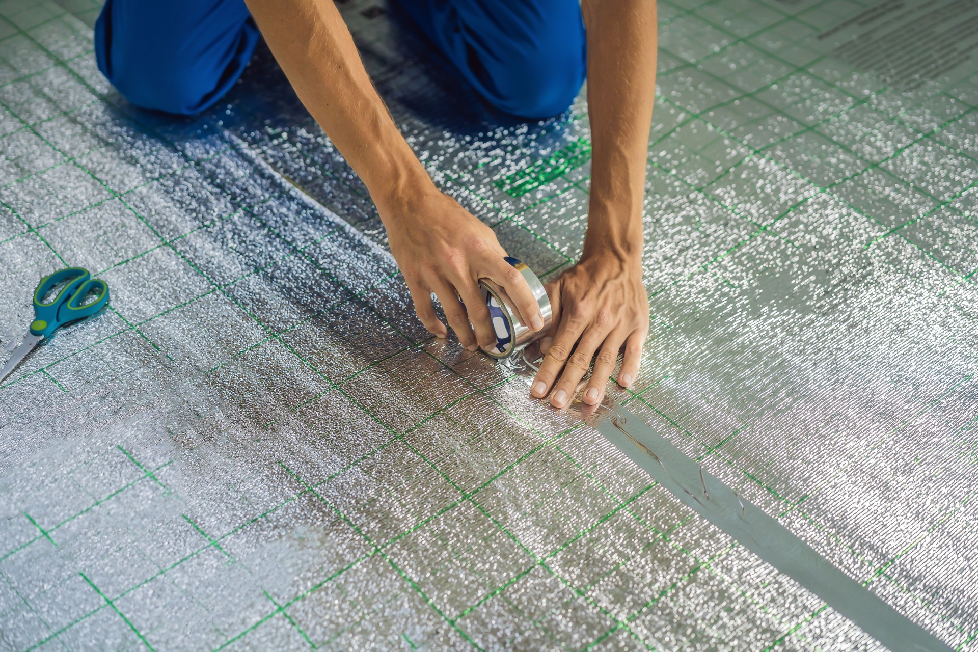 Master installs the overlapping thermal insulation in the room. Floor heating installation. Male hand holds reinforced tape. Repair in the apartment, floor insulation